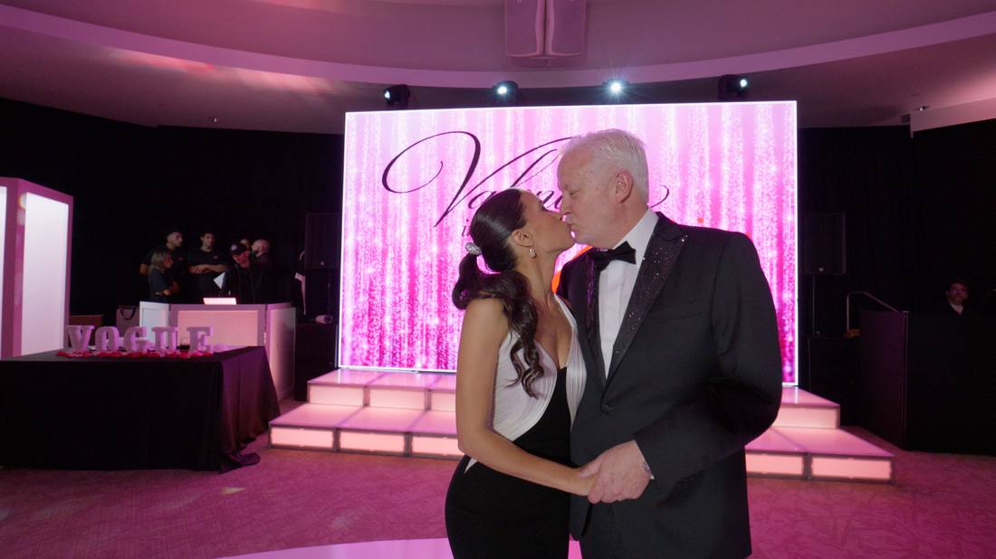 Couple sharing a kiss in front of a sparkling pink stage backdrop