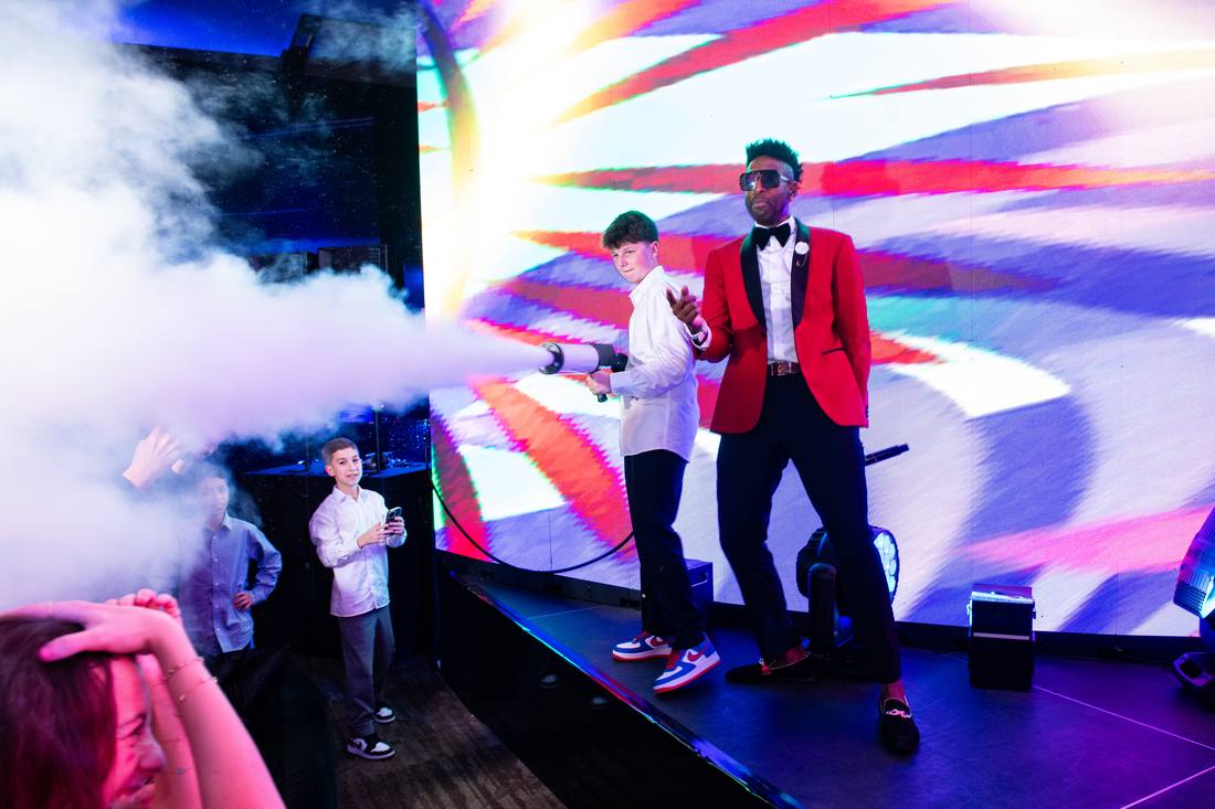 Emcee in a red blazer performing on stage with a young guest amid stage fog