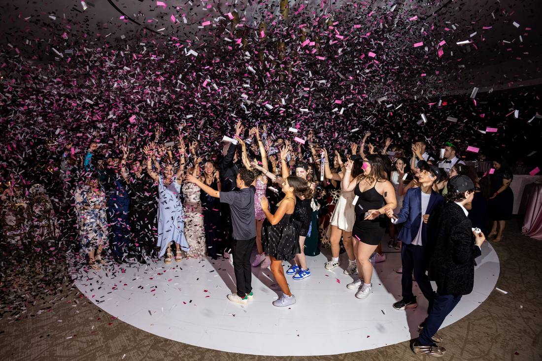 Guests dancing on the reception floor as pink and black confetti falls