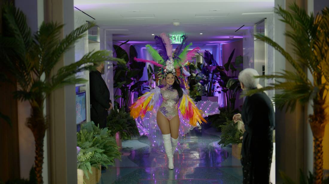 Costumed carnival performer walking through a palm-lined hallway entrance